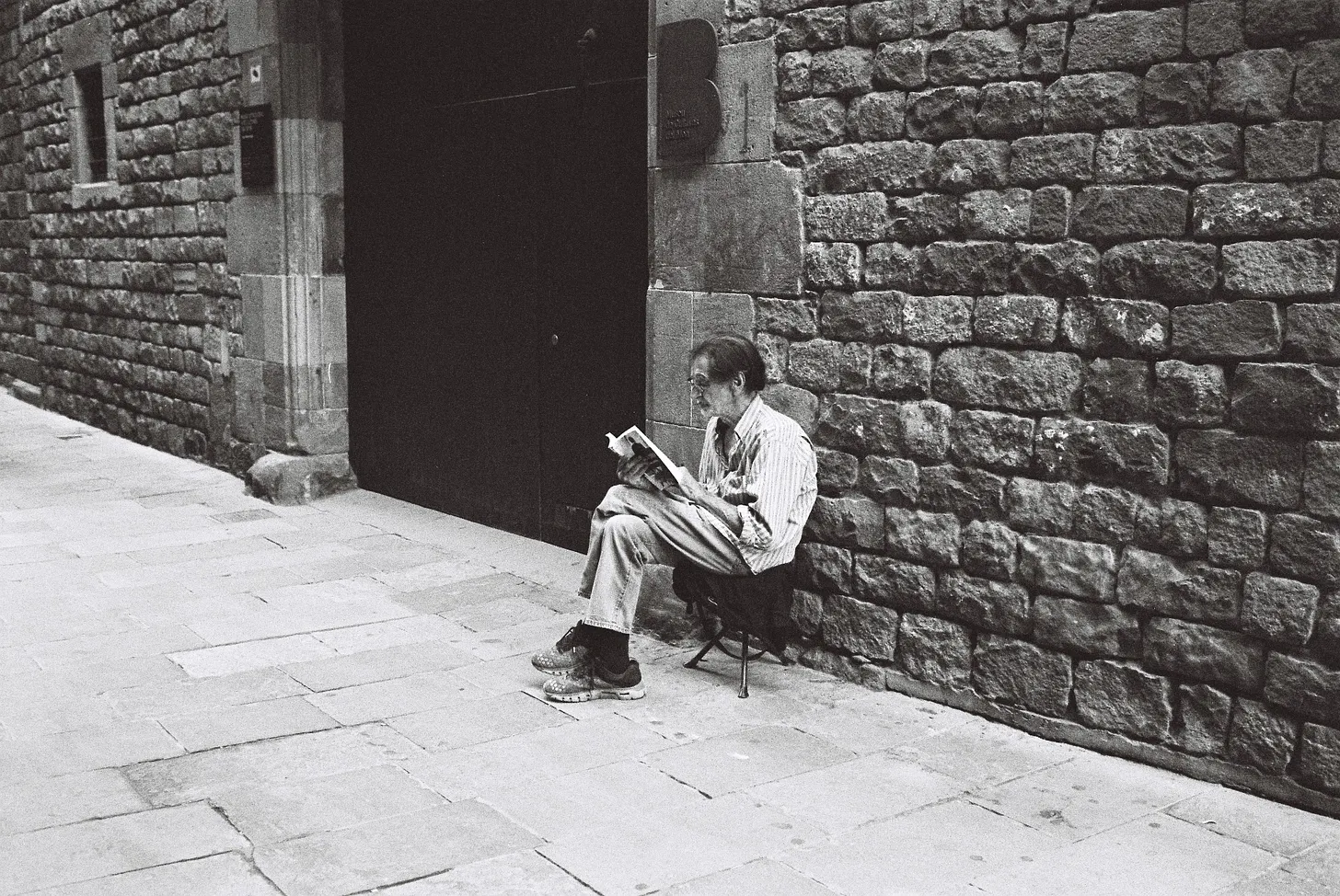 Enjoying the moment. A street vendor selling small antiques sits, enthralled by his book as the world passes him by. El Born, Barcelona.